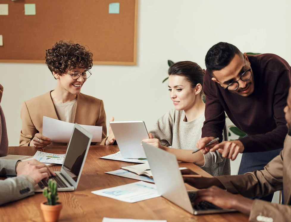 Collega's werken samen aan documenten en laptops tijdens een vergadering.