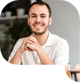 Man in witte polo glimlacht terwijl hij aan een tafel zit in een moderne, lichte ruimte.