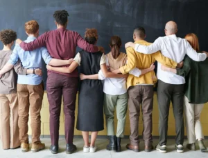 Groep mensen staat zij aan zij met de armen om elkaars schouders, gezien van achteren.