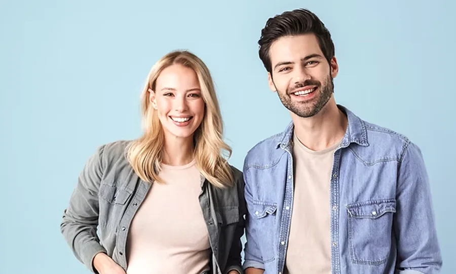 Twee lachende personen in casual kleding poseren voor een blauwe achtergrond.