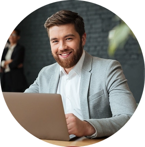 Hombre joven con barba trabajando en un portátil y sonriendo en una oficina del sector público.