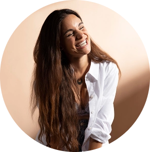 Mujer joven con camisa blanca sonriendo frente a un fondo beige.