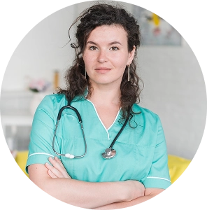 Female healthcare professional in scrubs with a stethoscope standing confidently with crossed arms.