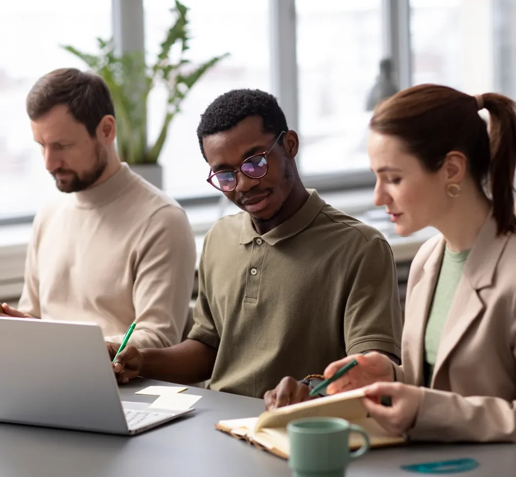 Drie collega’s zitten samen aan een bureau en bespreken werkdocumenten.
