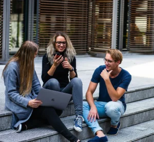 Drie jonge mensen zitten op een stoep en werken samen met een laptop en een smartphone.