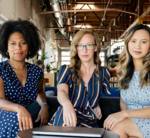 Drie vrouwen zitten in een moderne kantoorruimte en kijken ernstig in de camera.
