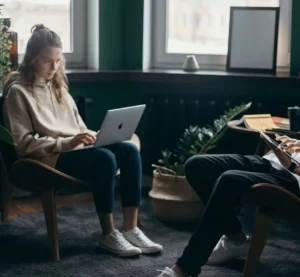 Twee mensen zitten tegenover elkaar terwijl een vrouw geconcentreerd op een laptop werkt.