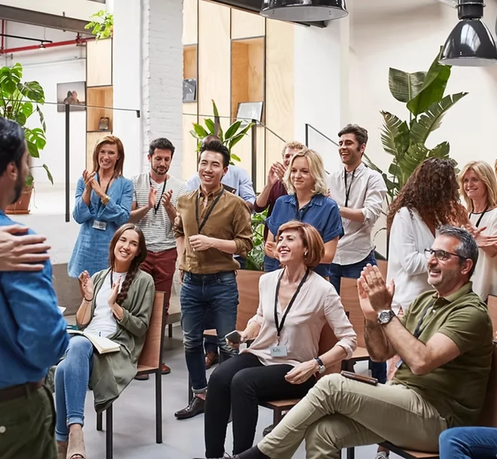 Een gemotiveerde groep collega’s luistert en applaudisseert tijdens een presentatie op kantoor.