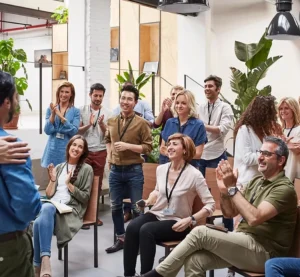 Een gemotiveerde groep collega’s luistert en applaudisseert tijdens een presentatie op kantoor.