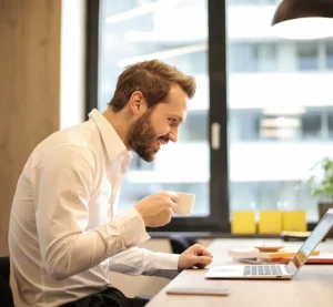 Man voert een Zoom-gesprek terwijl hij koffie drinkt aan zijn bureau.