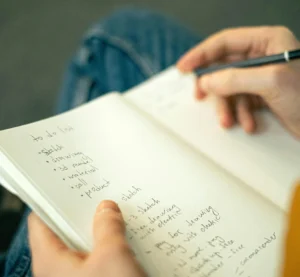 Close-up van handen die notities maken in een schrift met een to-dolijst.