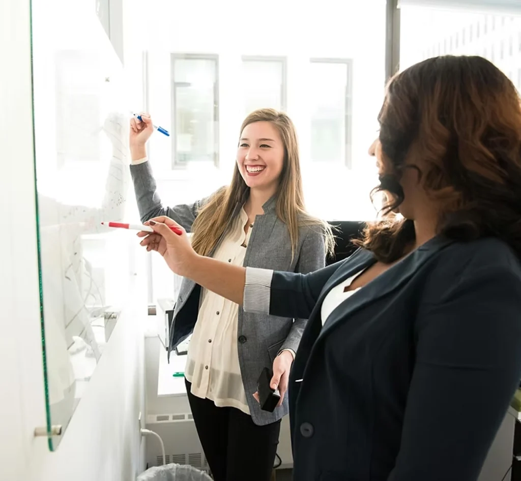 Twee collega’s schrijven en overleggen samen bij een whiteboard op kantoor.