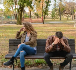 Twee gefrustreerde mensen zitten op een bankje in een park, elk met de blik van de ander afgewend.