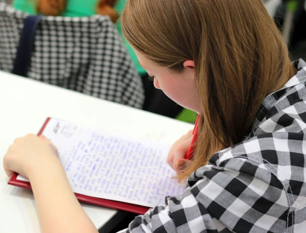 Vrouw met lang haar schrijft met een rode pen in een schrift tijdens het studeren.
