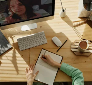 Persoon maakt aantekeningen in een notitieboek tijdens een Zoom-vergadering op een computer.