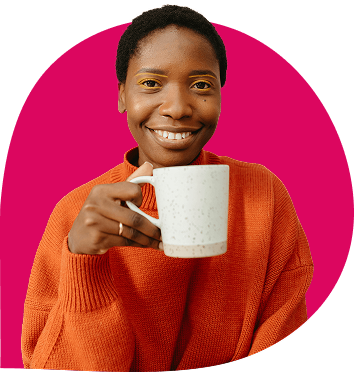 Vrouw met korte haren en oranje trui houdt lachend een witte mok vast voor een roze achtergrond.