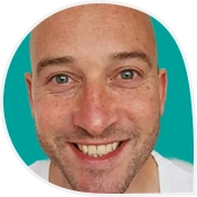 Portretfoto van een glimlachende man genaamd Douwe met een kale hoofdhuid en lichte ogen, voor een turquoise achtergrond.